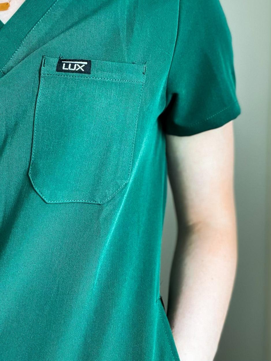 V-neck scrub top with a brand logo on the chest pocket and a tie at the waist.
