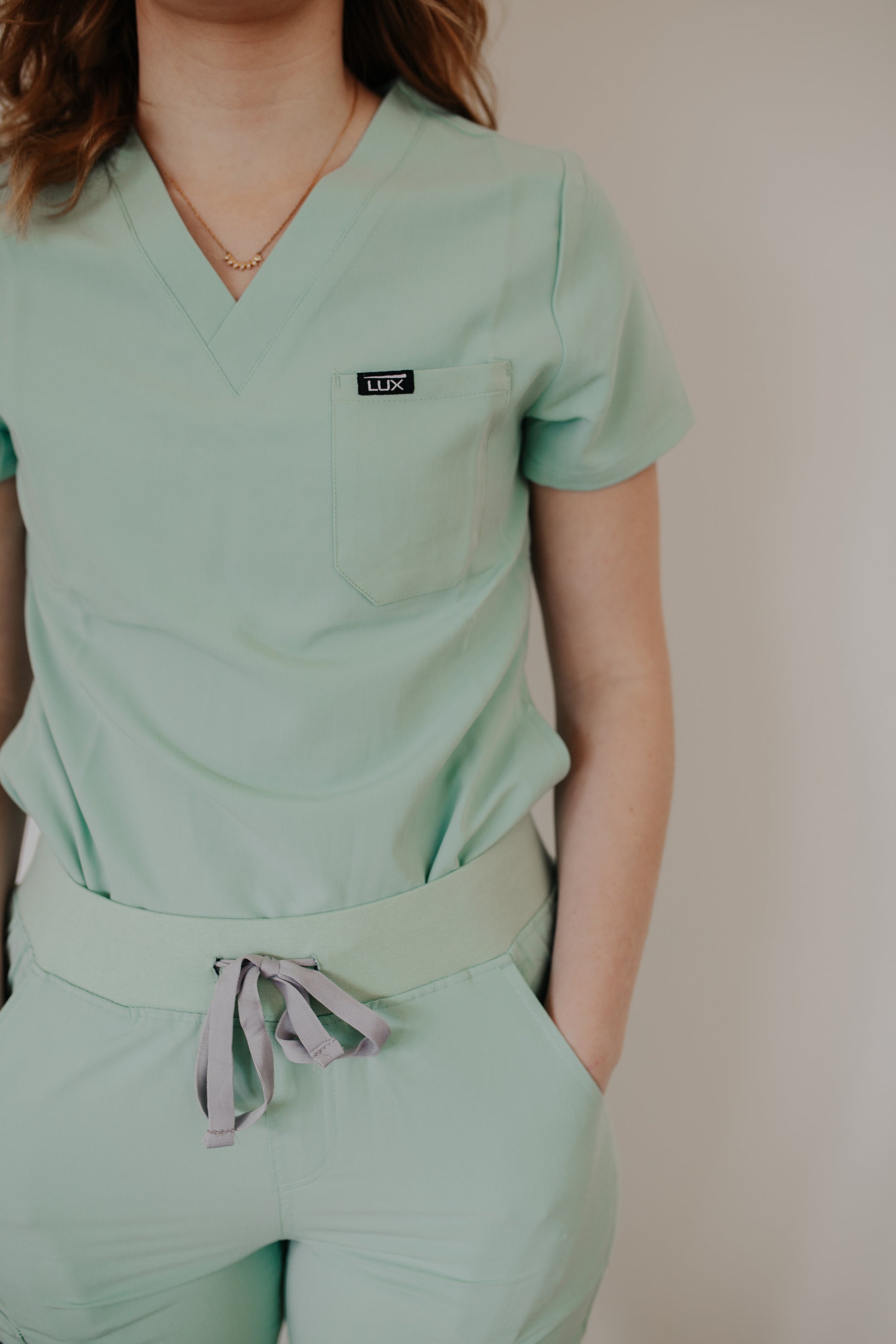 Person wearing a mint green scrub set with a visible brand logo against a plain background